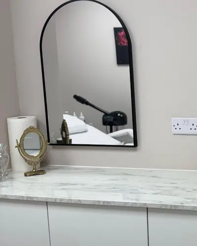 Treatment room with an arched black mirror, marble splashback and bronze basin