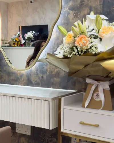 Manicure desk with a fluted white front, a backlit organic mirror, a gold ginkgo ornament and fresh flowers