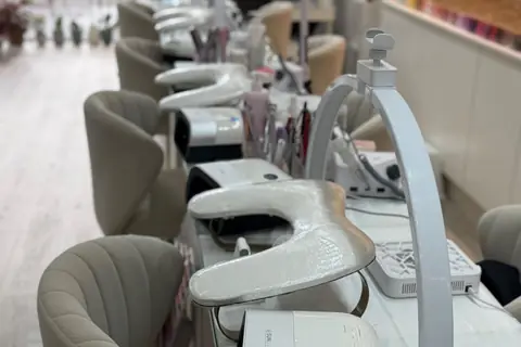Row of manicure tables with nail lamps and blush velvet chairs