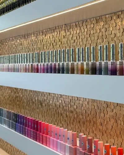 Rows of gel polish bottles in every colour on white shelves against Pari Beauty's gold hexagon-tiled wall